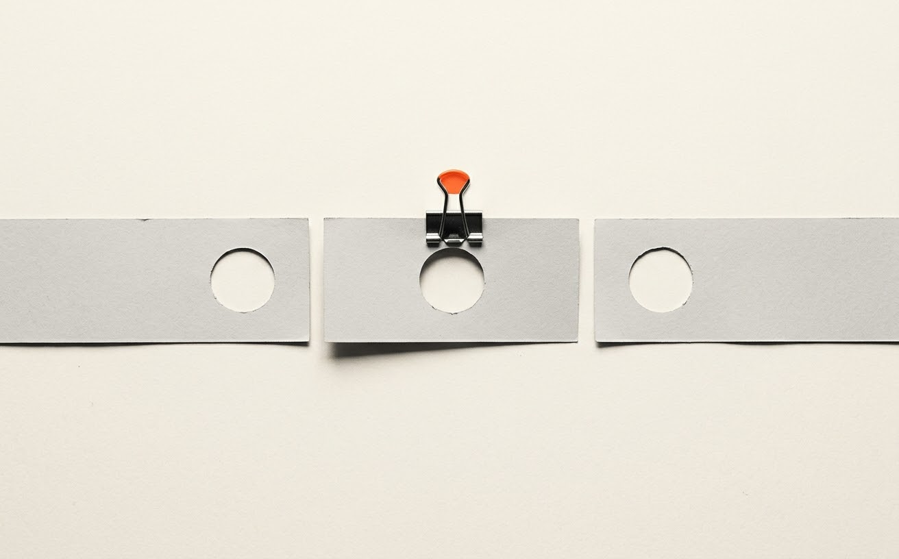 Three paper strips with punched holes, the middle one held by an orange binder clip