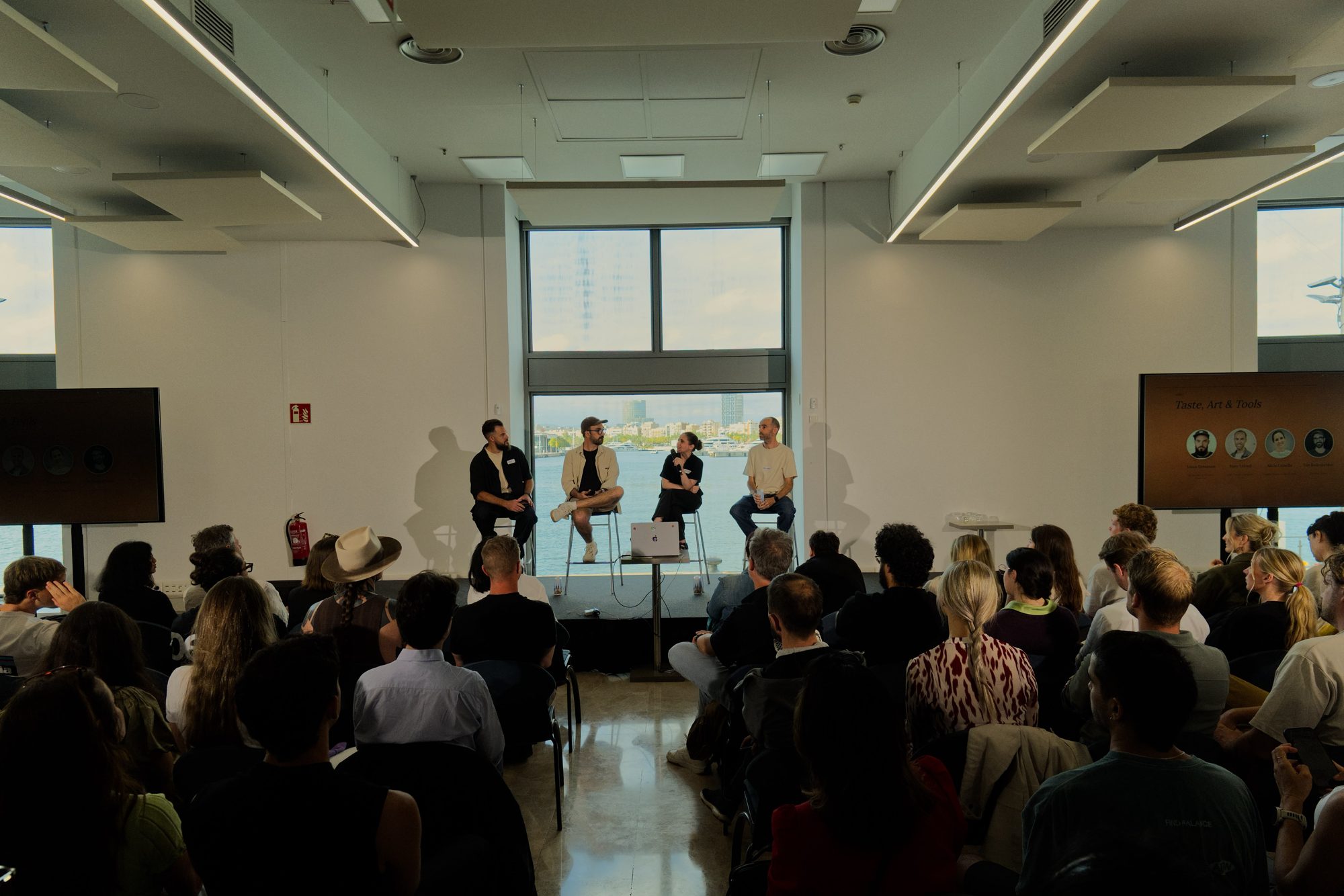 The four panelists seated on stools in front of a large window overlooking the sea, facing a packed audience, at Claude Community Barcelona #4, World Trade Center Barcelona